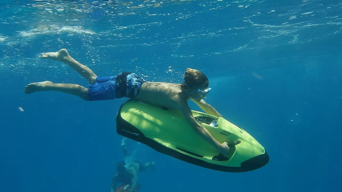 Rider gliding just under the surface on a green Seabob Super Dolphin in clear blue Maunalua Bay water