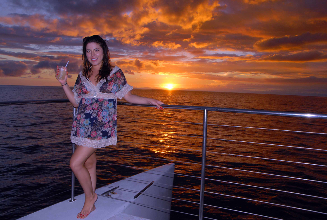 Guest watching a fiery Hawaiian sunset from the deck of the Kai Oli Oli catamaran
